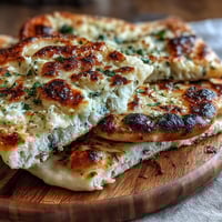 Freshly baked The Best Easy Garlic Naan Bread, golden-brown and bubbling, just pulled from a hot cast iron skillet.