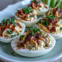 Classic Deviled Eggs with Paprika and Chives arranged on a white platter, garnished with smoky paprika and fresh chives for a vibrant appetizer.
